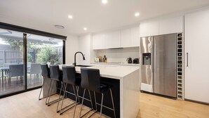 Una cocina moderna con una isla central, taburetes de bar, un refrigerador de acero inoxidable y un  puerta corrediza de vidrio que da a un espacio exterior.