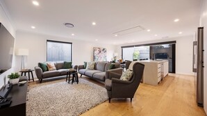 Una sala moderna con sofá, sillón y mesa de centro, una zona de cocina con refrigerador y pileta, y un comedor con sillas.