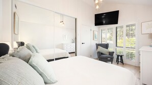 Un dormitorio con una cama grande, una silla, un televisor y un ventanal con persianas.