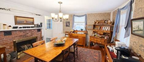 A traditional kitchen with a brick fireplace, wooden dining table, and a chandelier.