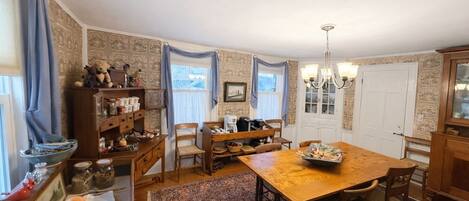 A traditional dining room with a wooden table, chairs, and a chandelier. There is a window with curtains, a door, and a patterned wallpaper.
