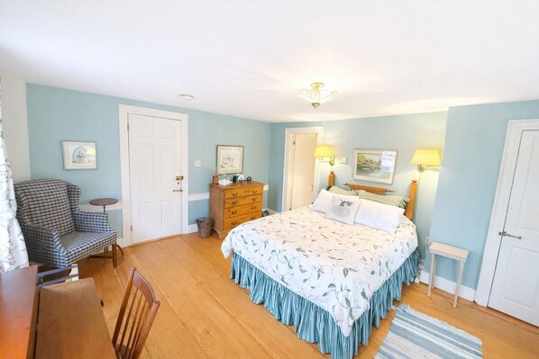 A bedroom with a bed, dresser, chair, and two doors.