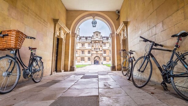 A corridor with two bicycles parked on either side, leading to a large building with a clock tower. - Modern ensuite Studio Retreat off Vibrant Mill Rd (Cambridge)