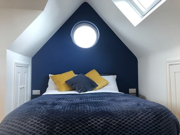 A bedroom with a sloped ceiling, a round skylight, a bed with a patterned bedspread, and two pillows. - Modern ensuite Studio Retreat off Vibrant Mill Rd (Cambridge)