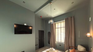 Een slaapkamer met een bed, een aan de muur bevestigde televisie, een raam met gordijnen en een plafondlamp.