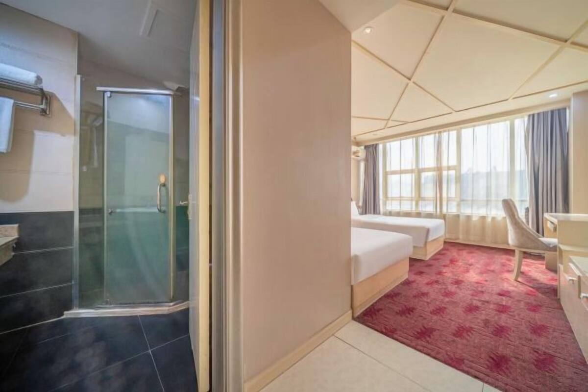 A hotel room with a bed, a desk, a chair, a shower, and a window.