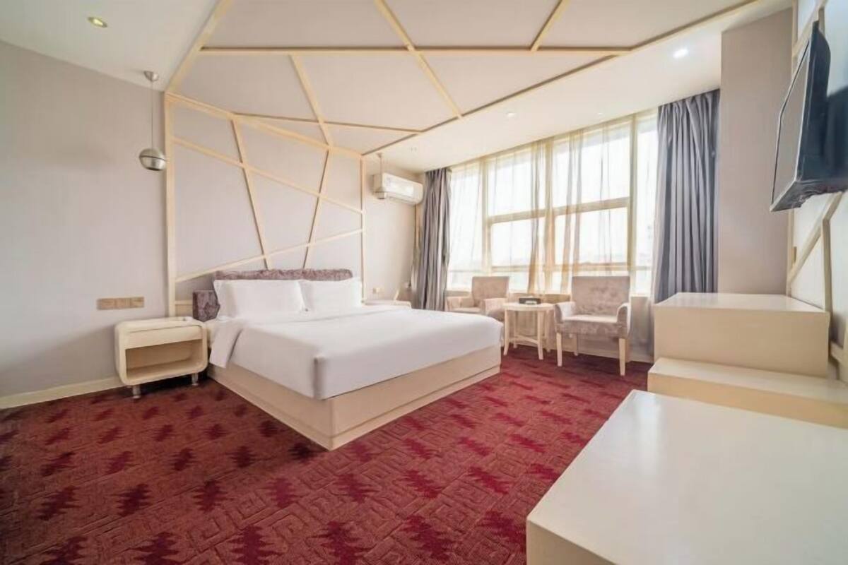 A hotel room with a bed, a desk, a chair, a TV, and a window with curtains.