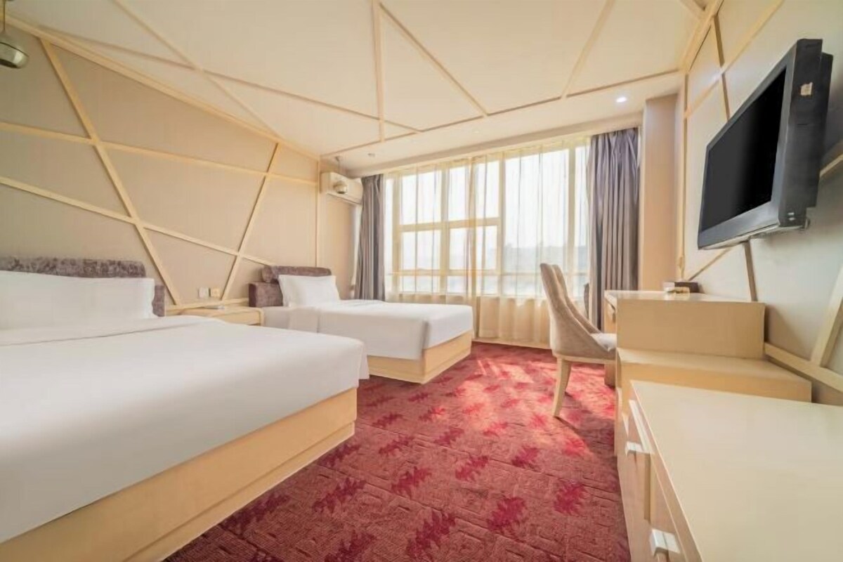 Ein Hotelzimmer mit zwei Betten, einem Schreibtisch, einem Fernseher und einem großen Fenster mit Vorhängen.