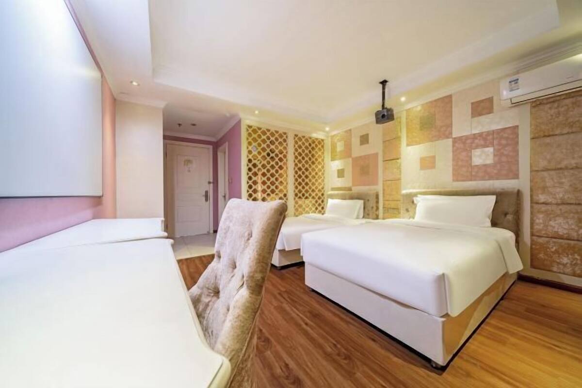 A hotel room with two beds, a chair, a wooden floor, and a patterned wall.