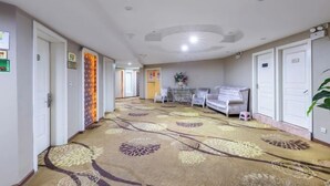 A hotel corridor with a patterned carpet, a sofa, a small table, and a plant. - Tuk China Light Residence Hotel (Taizhou Luqiao Airport Branch) (Taizhou)