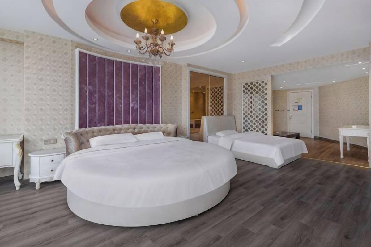 A bedroom with a large round bed, a separate bed, a nightstand, a dresser, and a chandelier.