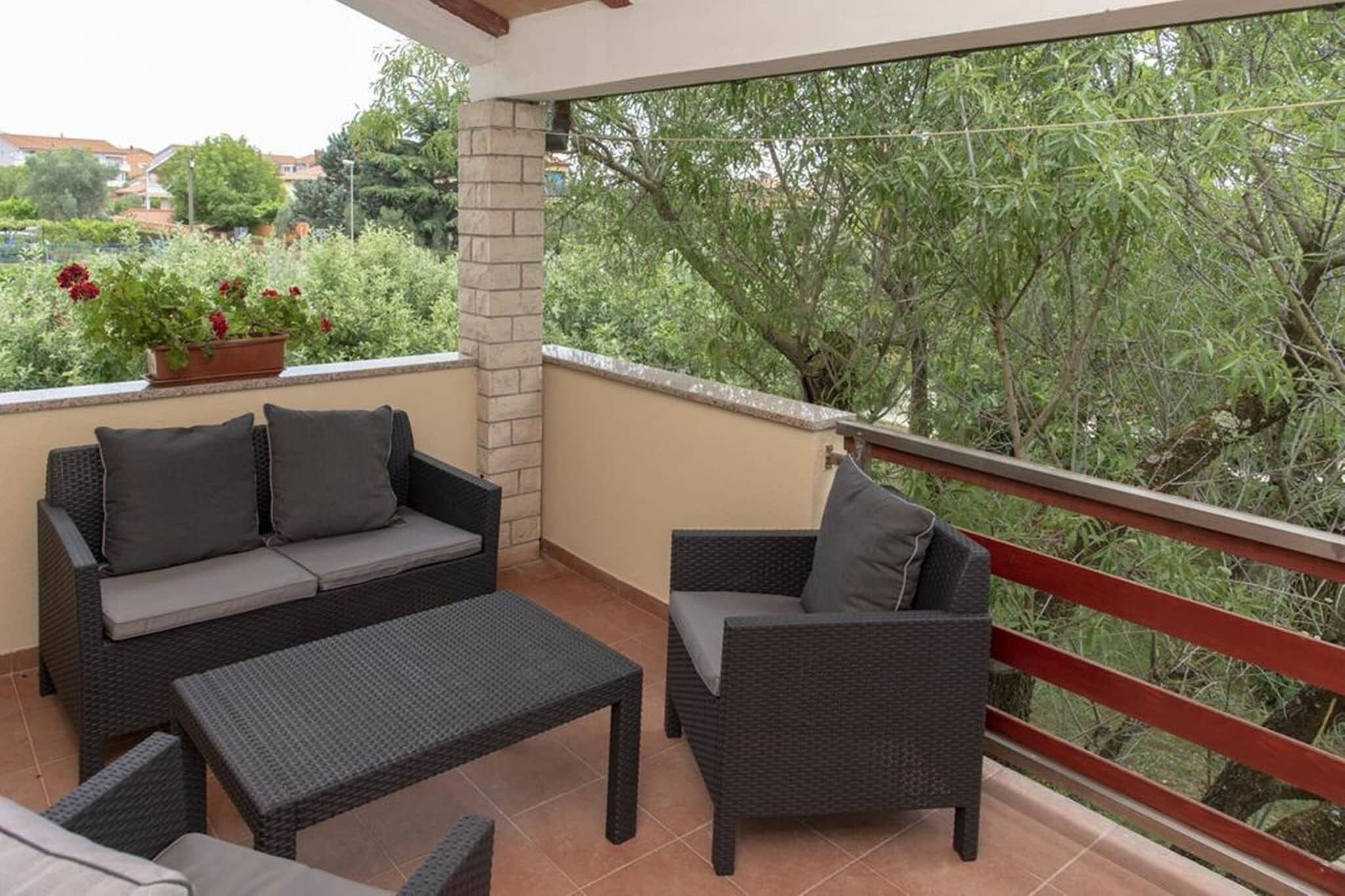 A balcony with wicker furniture, a potted plant, and a view of trees and buildings.