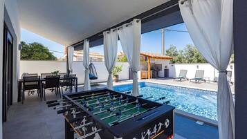 Ein Poolbereich mit Tischfußball, Sitzgelegenheiten im Freien und Blick auf den Pool.