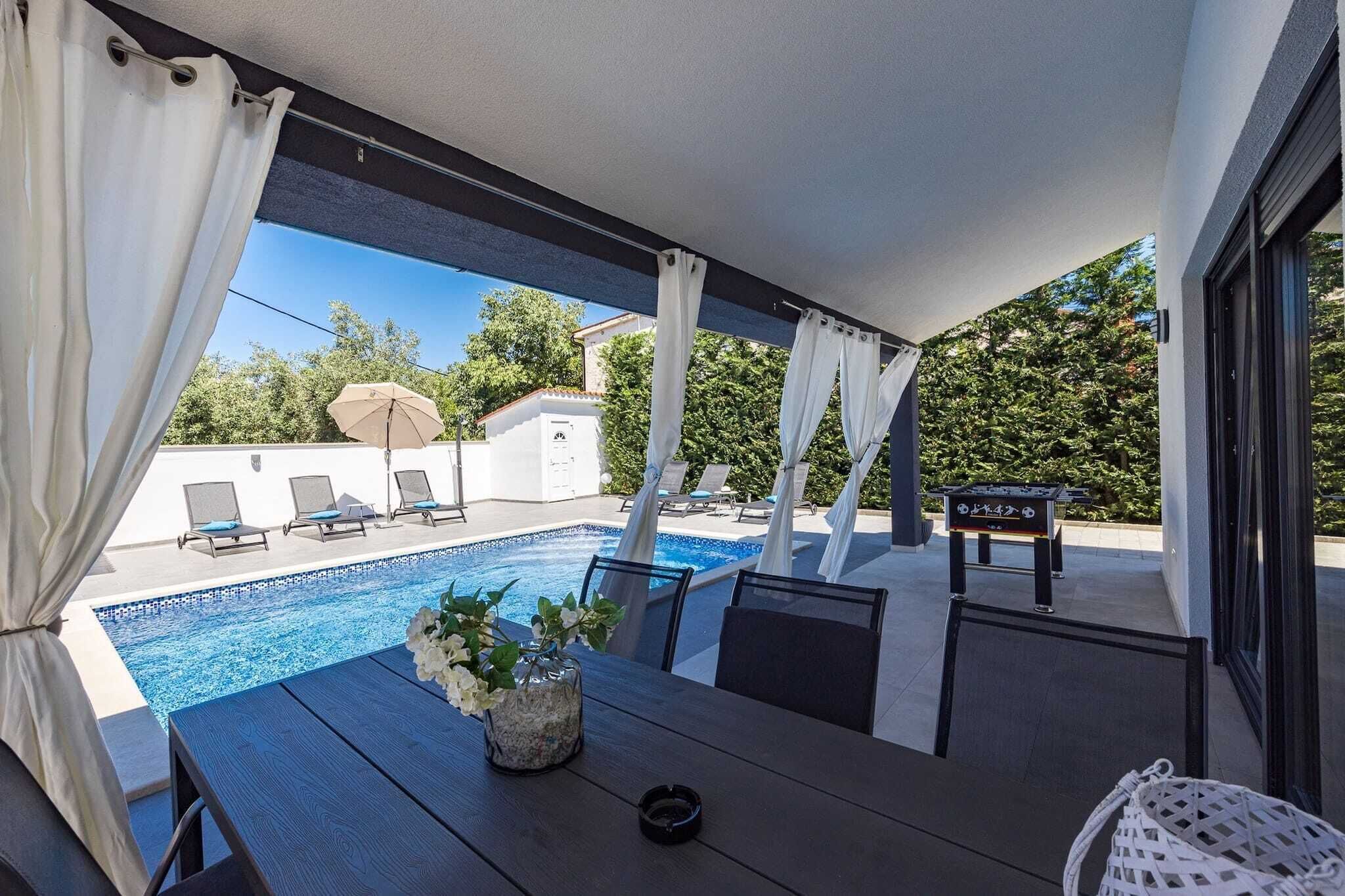 Ein überdachter Außenbereich mit Pool, Liegestühlen und einem Tisch mit Blumen.