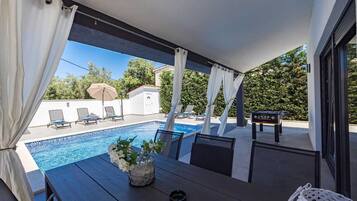 Ein überdachter Außenbereich mit Pool, Liegestühlen und einem Tisch mit Blumen.