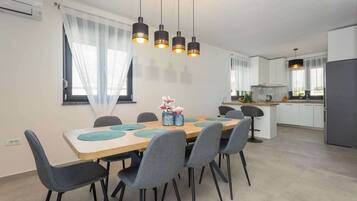 Eine moderne Küche mit weißen Schränken, einem grauen Kühlschrank und einem Essbereich mit Holztisch und grauen Stühlen.
