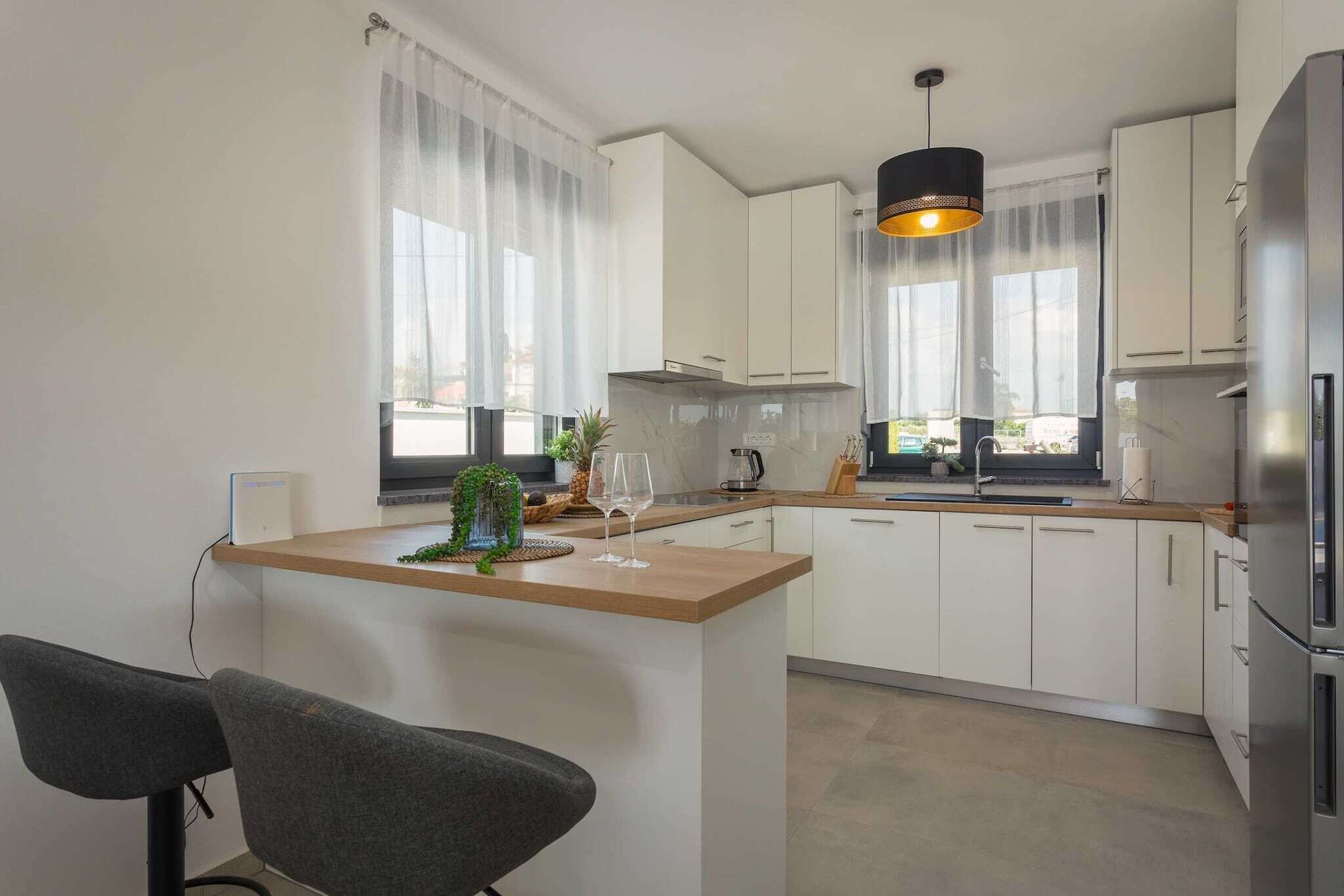 Eine moderne Küche mit weißen Schränken, einer Holz Arbeitsplatte und einer schwarzen Pendelleuchte.