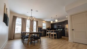 Una cucina moderna con mobili scuri, una zona pranzo con tavolo e sedie in legno, e un'ampia finestra con tende.