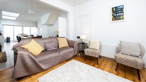 A modern living room with a brown sofa, patterned armchairs, a white rug, and a painting on the wall.