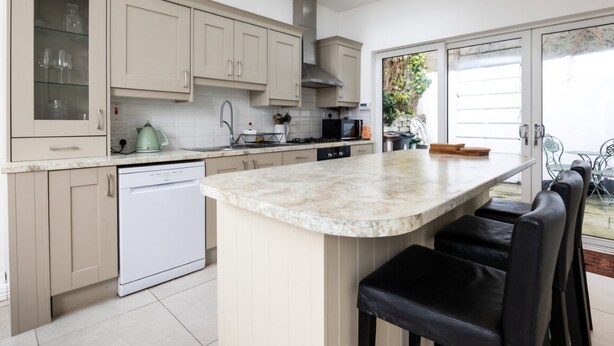 A modern kitchen with a dishwasher, a large island with bar stools, and a view of the outdoor patio area.