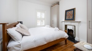 A bedroom with a wooden bed, white bedding, a fireplace, and a framed artwork on the wall.