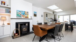 A modern kitchen with a dining area, white cabinetry, a fireplace, and a large window.