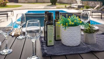 A poolside table with wine glasses, bottles of San Antonio olive oil, and potted plants.