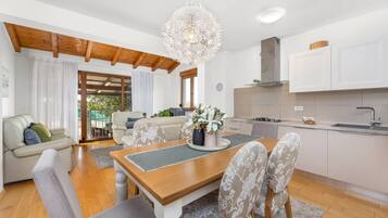A modern kitchen with white cabinets, a wooden dining table, and a chandelier.