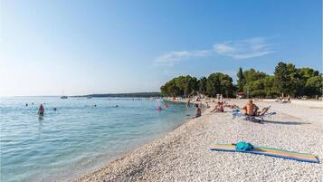 A pebbled beach with people sunbathing and swimming.