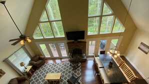 A spacious living room with a fireplace, large windows, a wooden dining table, and a cozy seating area. - Family Friendly Mountain Getaway with Theater & Arcade in the Laurel Highlands (Somerset)