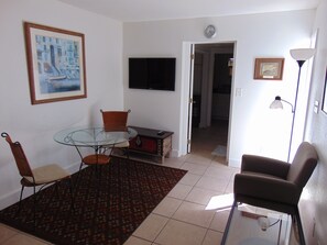 Ein Wohnzimmer mit Glastisch, zwei Stühlen, Fernseher, Uhr und Lampe.