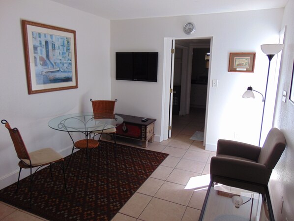A living room with a glass table, two chairs, a TV, a clock, and a lamp.