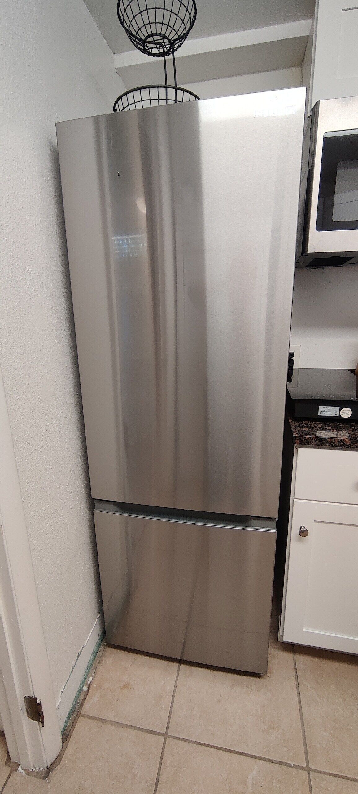 A stainless steel refrigerator in a kitchen with white cabinets and a microwave above it.