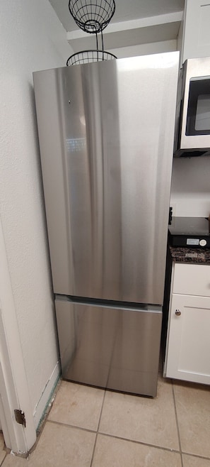 Ein Edelstahl-Kühlschrank in einer Küche mit weißen Schränken und einer Mikrowelle darüber.