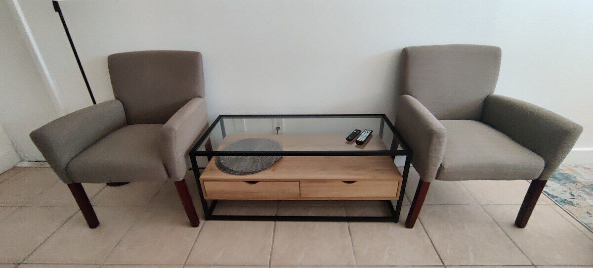 Ein Zimmer mit einem Glastisch, zwei Sesseln und einem Holztisch.