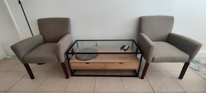 Ein Zimmer mit einem Glastisch, zwei Sesseln und einem Holztisch.