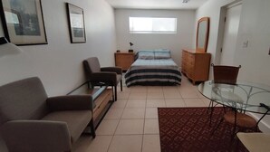 Een kleine slaapkamer met een bed, een slaapbank, een glazen tafel en een dressoir.