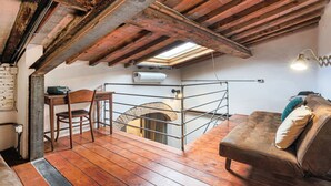 Een knus zolderkamertje met zichtbare houten balken, een hoogslaper, een bureau met stoel en een bank.
