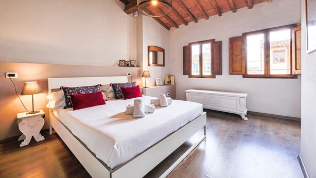 Een slaapkamer met een groot bed, houten balken, een radiator en een raam met luiken.