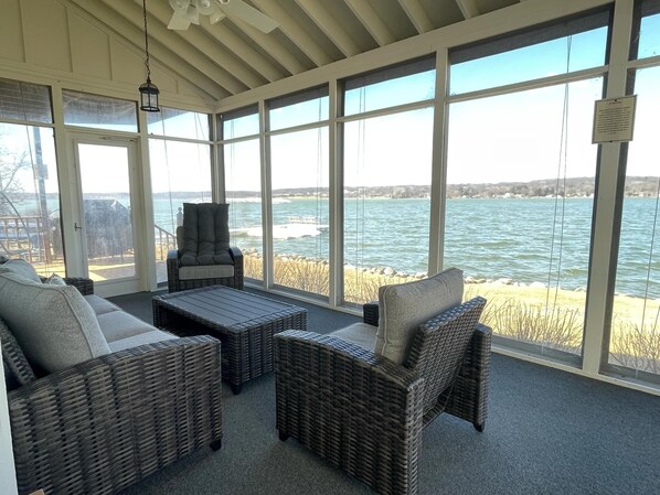 A sunroom with wicker furniture, large windows, and a view of the water. - Waterfront Lake House with game room, private pier and kayaks in Lake Geneva (Lake Geneva)