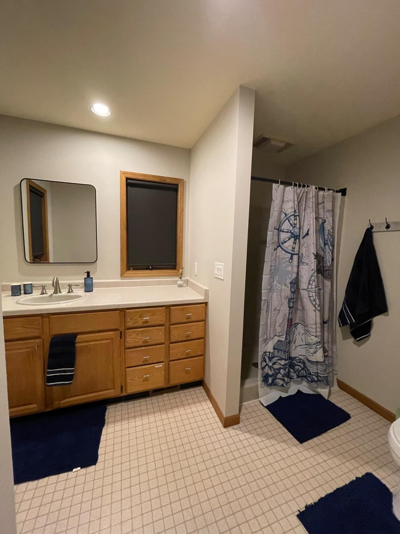Une salle de bain avec un lavabo, un miroir, des meubles en bois et un rideau de douche orné de motifs marins.