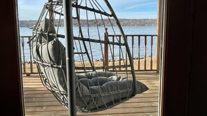 A wooden deck with a hanging chair facing a body of water. - Waterfront Lake House with game room, private pier and kayaks in Lake Geneva (Lake Geneva)