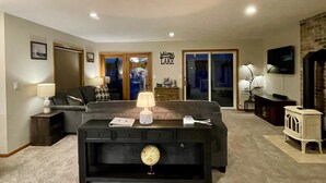 A living room with a sofa, coffee table, and a TV. There is a door leading to a balcony and a sign that says "Welcome Lake". - Waterfront Lake House with game room, private pier and kayaks in Lake Geneva (Lake Geneva)