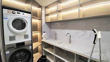 A compact hotel bathroom with a built-in washer and dryer, a sink with a handheld showerhead, and a marble-tiled vanity.