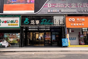 Fachada con un letrero que dice 'Dragon Palace Deluxe Hotel' y tiendas adyacentes.