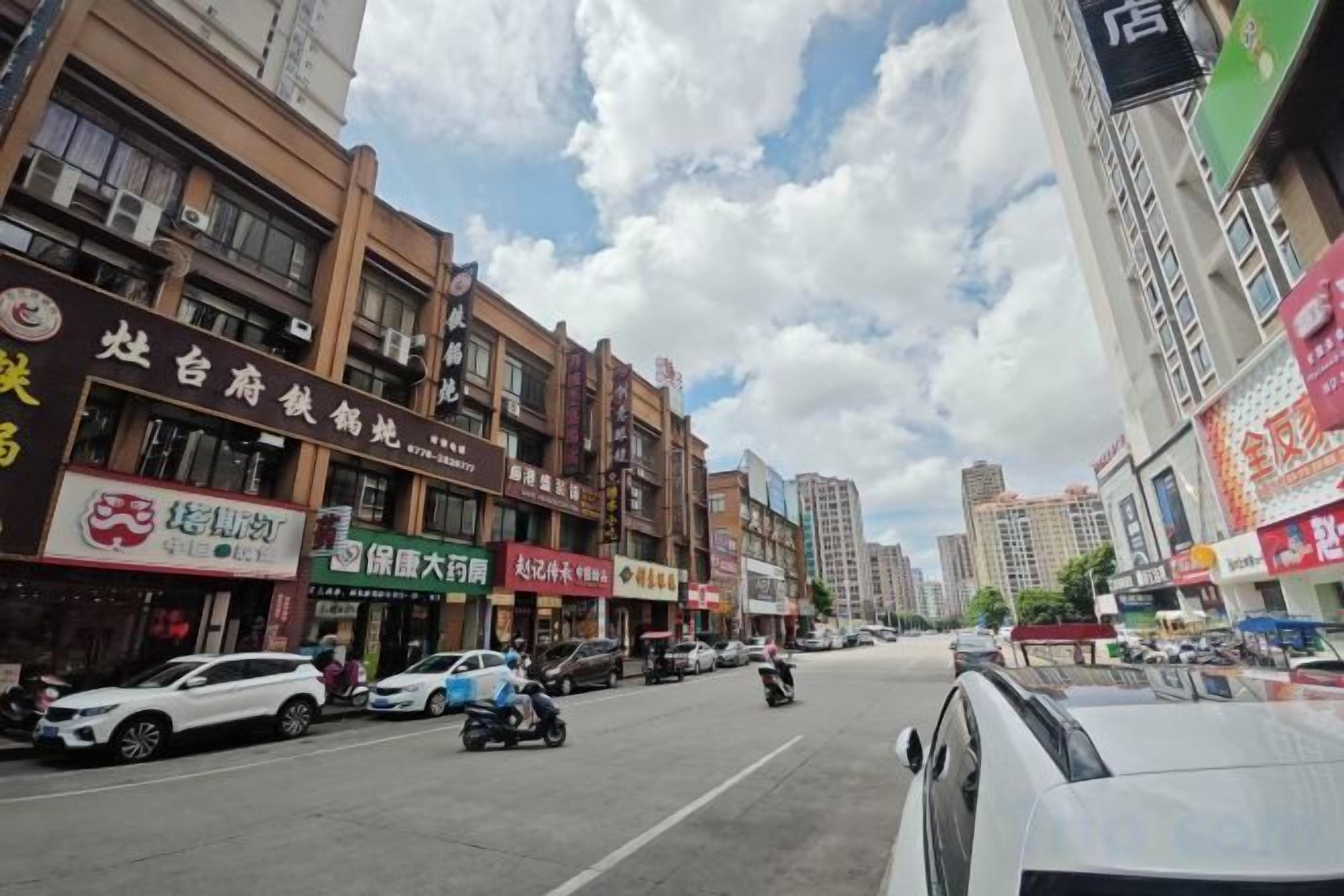 Vista de la calle con varios edificios comerciales, automóviles y una motocicleta.