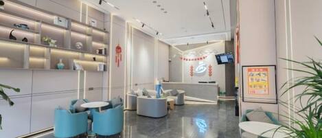 A modern hotel lobby with a reception desk, seating area, and decorative plants.