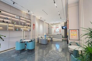 Un moderno vestíbulo de hotel con una recepción, zona de estar y plantas decorativas.