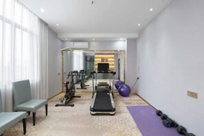 Een fitnessruimte met loopband, hometrainer en losse gewichten.