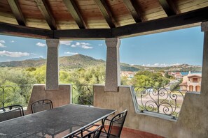 Un espacio al aire libre techado con una mesa y sillas, y vistas a un paisaje montañoso, con barandilla.